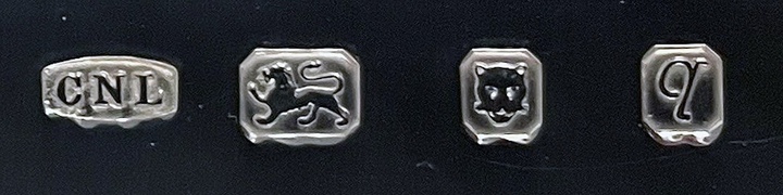 Les quatre poinçons de l'Atmos Christopher Lawrence, modèle A (Patrimoine Jaeger-LeCoultre, inv. 2154). Obligatoires sur tout objet en argent britannique, ils se lisent de gauche à droite: C·N·L, le poinçon de l'orfèvre Christopher Nigel Lawrence; le lion passant, qui garantit l'argent sterling à 925 millièmes; la tête de léopard, sans couronne depuis 1821, marque du bureau de garantie de Londres; et la lettre-date, qui identifie l'année du poinçonnage.