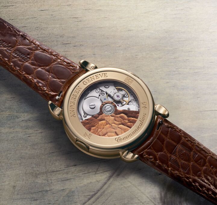 Pour marquer son 45ème anniversaire, Andersen Genève a créé la Communication 45, une montre à heure universelle en édition limitée qui célèbre le statut emblématique de cette complication dans l'histoire de la marque (image du haut, à côté de la montre Communication de 1990). La fonction heure universelle est assurée par un module d'une épaisseur de seulement 0,9 mm, constamment perfectionné depuis sa création en 1990. Comme du côté cadran, la masse oscillante est en or bleu 21ct couleur cognac. Les ponts et le coq ont une finition «frosted» qui fait ressortir le délicat anglage du mouvement. 